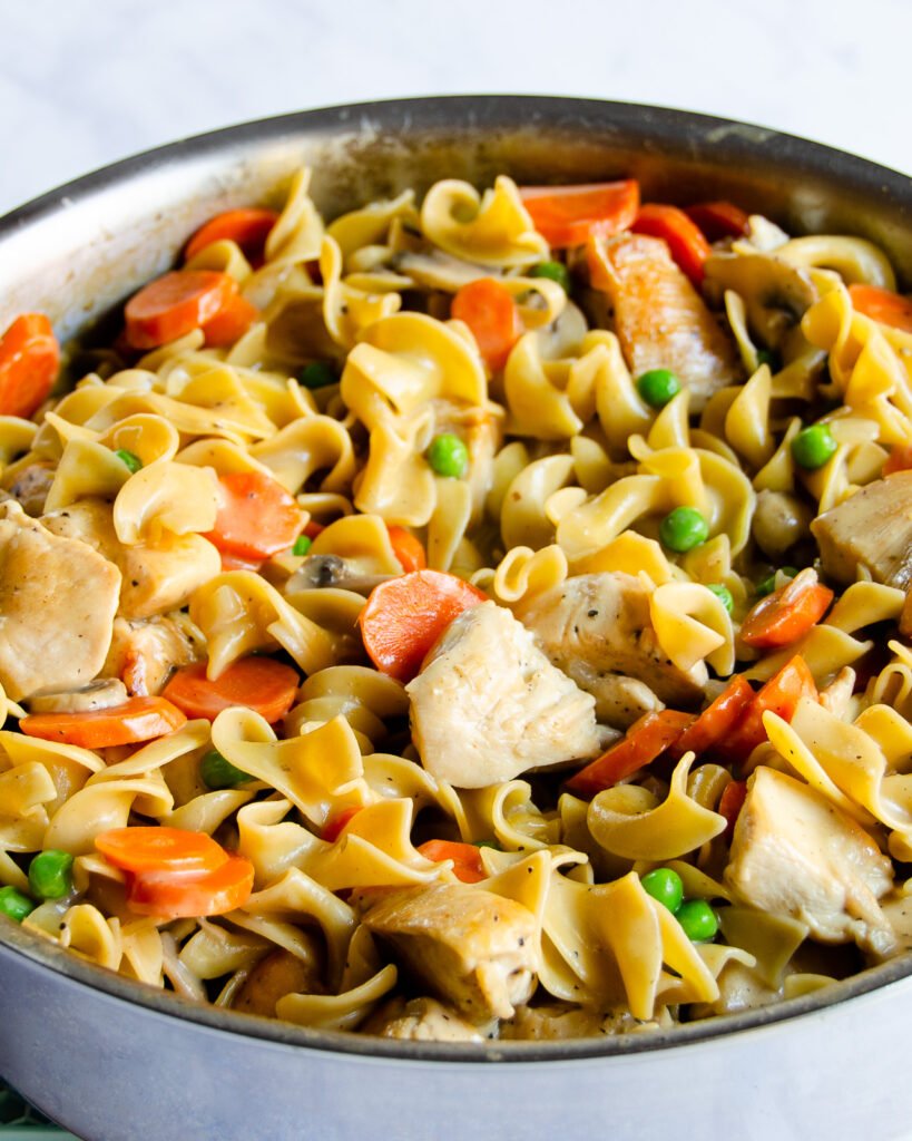 Creamy Tarragon Chicken with Egg Noodles in a stainless steel saute pan.