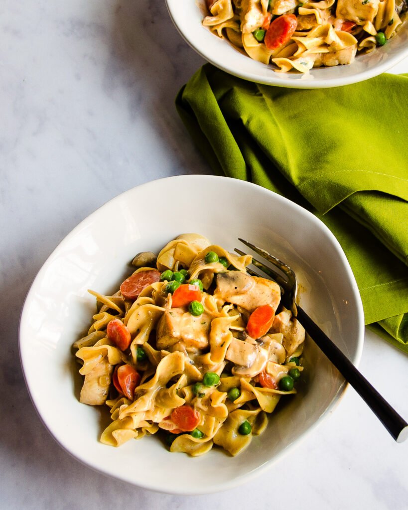 A bowl of chicken and egg noodles with a fork and a green napkin.
