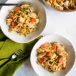 Two bowls of creamy tarragon chicken and egg noodles on a countertop with a saute pan in the background.