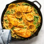 Lemon Chicken Skillet Dinner with spinach and orzo in a cast iron skillet on a counter with a towel wrapped around the handle.