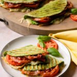 Italian BLT Panini on a plate with two more paninis on a cutting board in the background.