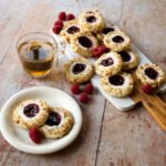 Raspberry Cream Cheese Thumbprint Cookies on aa wooden board and a small plate with a cup of tea.