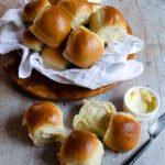 Sheet Pan Dinner Rolls in a linen-lined basket and on a wooden table.