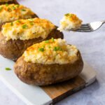 Boursin Twice Baked Stuffed Potatoes on a wooden board with a fork scooping out some of the potato.