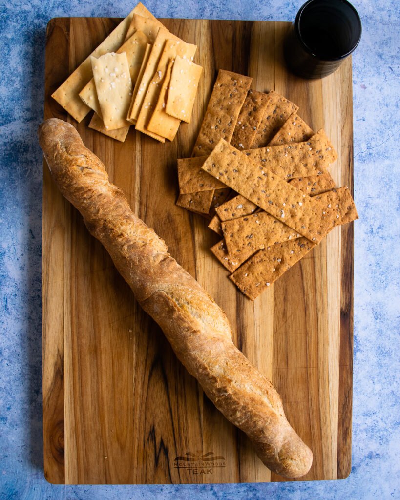 A baguette and crackers on a cutting board.