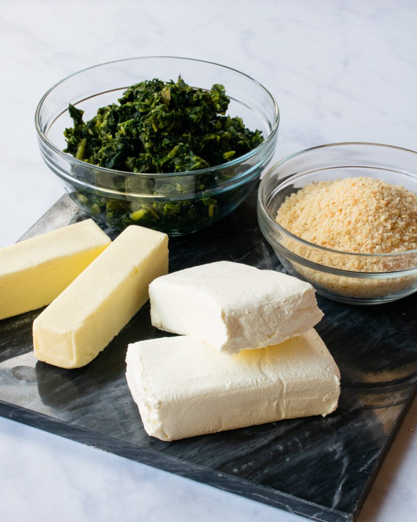 Ingredients for creamed spinach casserole - spinach, butter, cream cheese and breadcrumbs - on a marble counter.