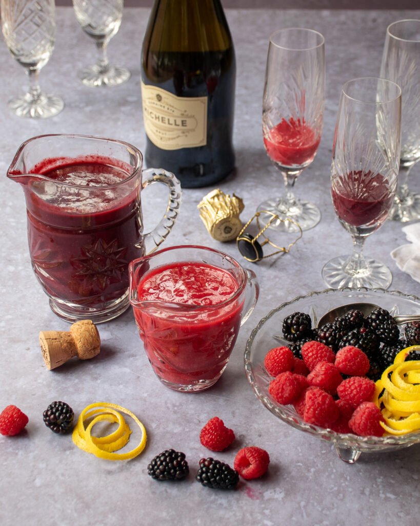 All the ingredients for jam bellinis with two champagne flutes being filled.