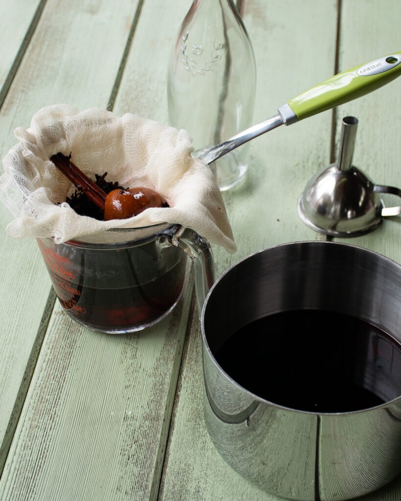 Straining brewed sorrel from a saucepan through cheesecloth into a measuring glass.