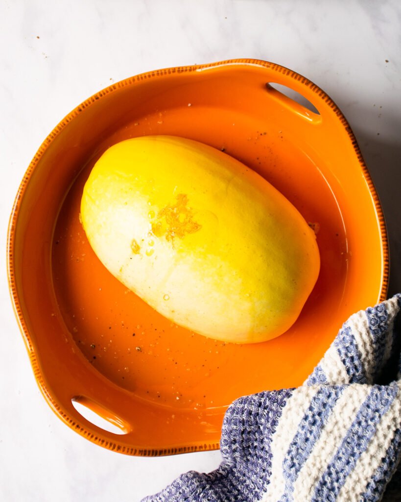 Half a spaghetti Squash in an orange ceramic dish with a blue and white striped towel.
