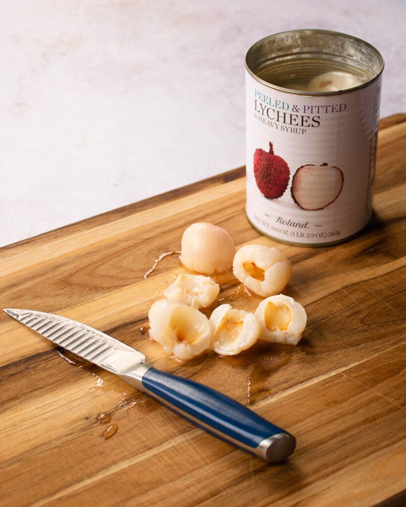 A can of lychees on a cutting board with a paring knife.
