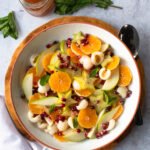 Winter Fruit Salad in a white bowl with fresh mint and a jar of dressing near by.