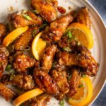 Air Fried Orange Sesame Chicken Wings on a white platter with slices of orange and sliced scallions garnishing the plate.