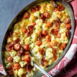 Cauliflower Alfredo Bake in an oval gratin dish on a counter with a red towel wrapped around the pan and a spoon sticking out.