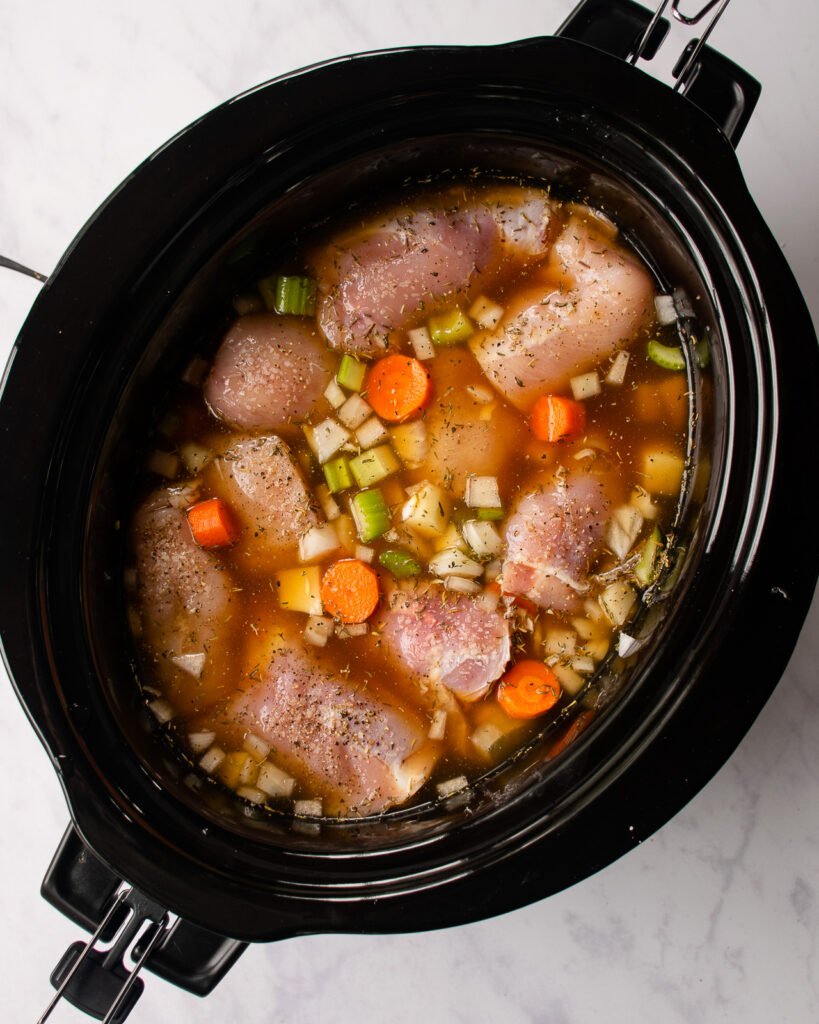 Raw chicken breasts and vegetables in aa slow cooker covered with broth.
