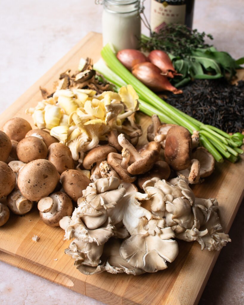 A wooden cutting board with soup ingrediens - a variety of mushrooms, celery, shallots, cream, sherry, herbs and wild rice.