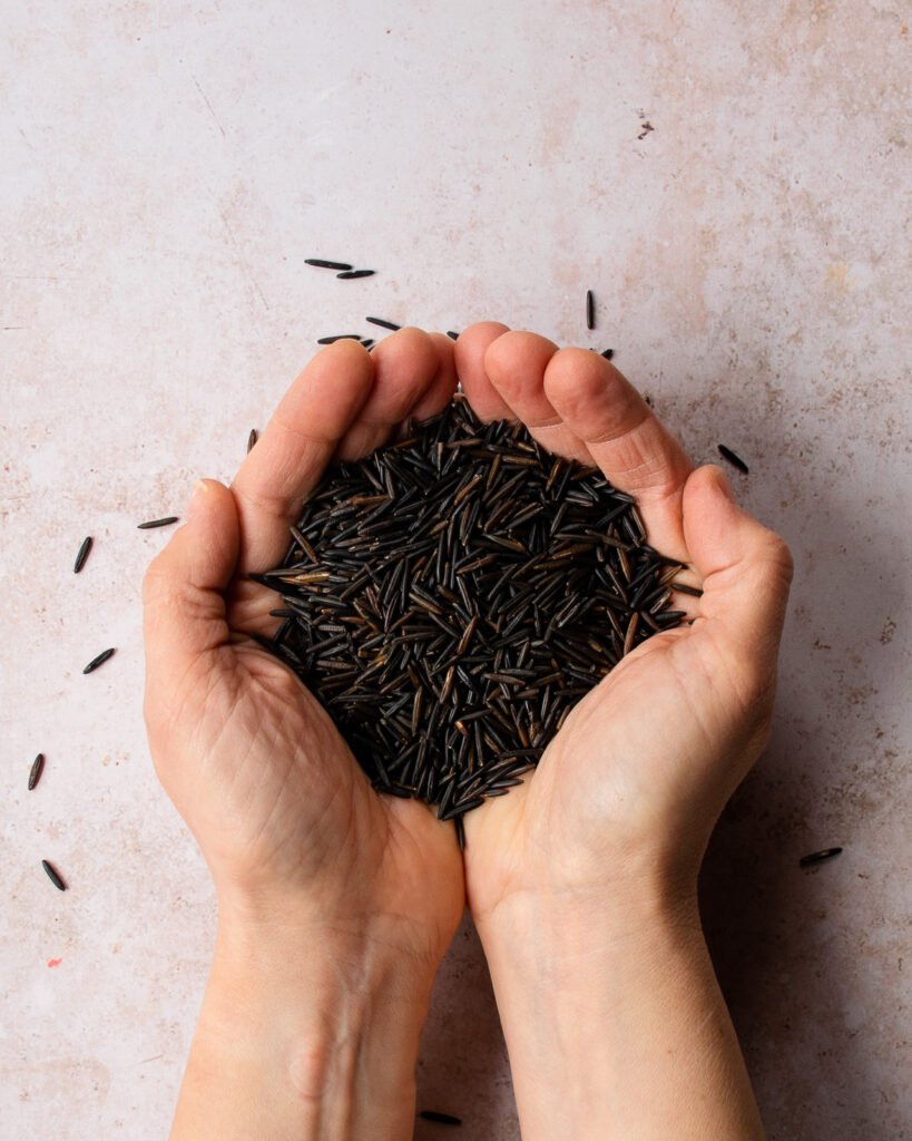 Two hands holding a handful of raw wild rice.