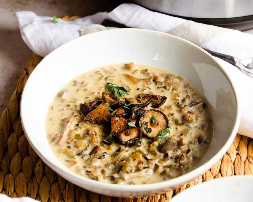 A bowl of cream of mushroom soup on a rattan mat with napkin and spoon.