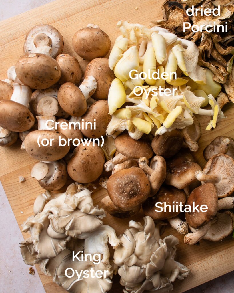 A wooden cutting board with different varieties of labeled mushrooms.