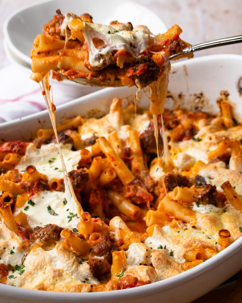 A spoon lifting some ziti al forno out of the ceramic casserole dish.