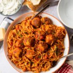 A large serving bowl of spaghetti and meatballs with some crusty bread and whipped ricotta near by.