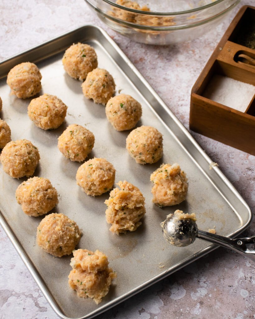 Chicken meatballs on a sheet pan with an ice cream scoop resting on the side.