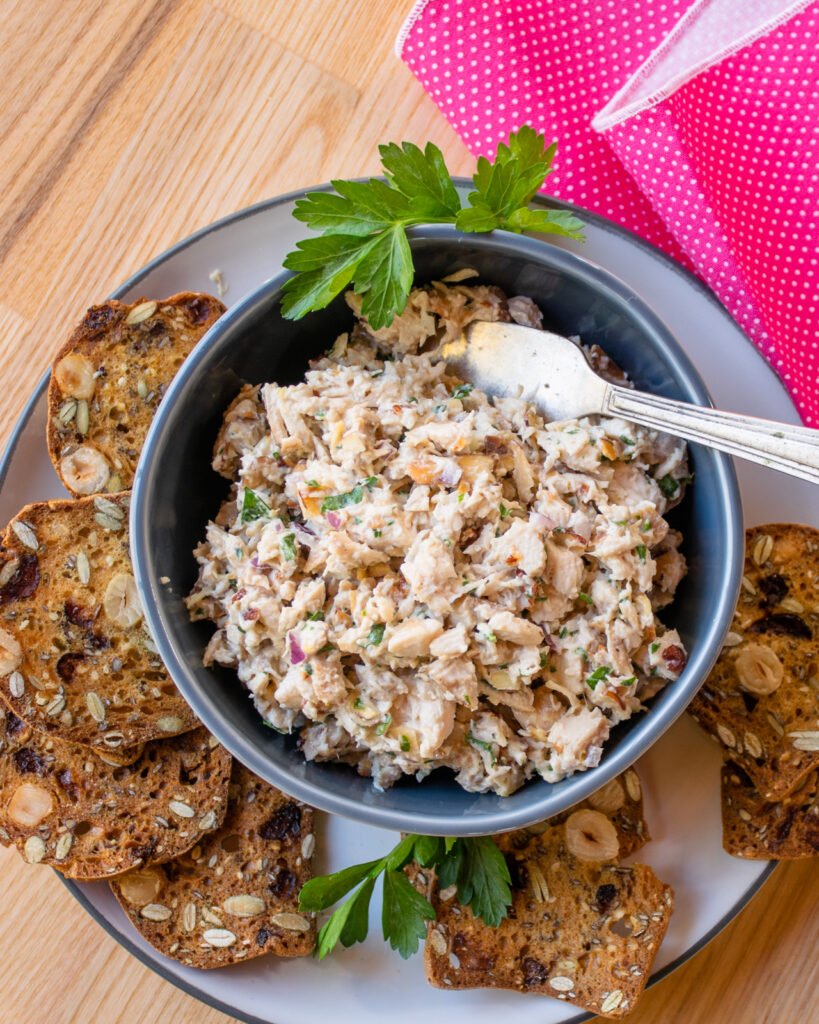 A bowl of chicken salad with crackers around it and a pink napkin.