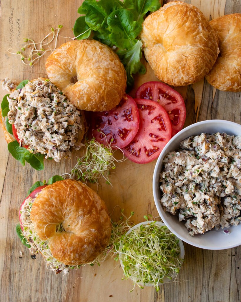 Looking straight down on a cutting board with croissants, chicken salad, tomatoes and lettuce - building chicken salad croissant sandwiches.