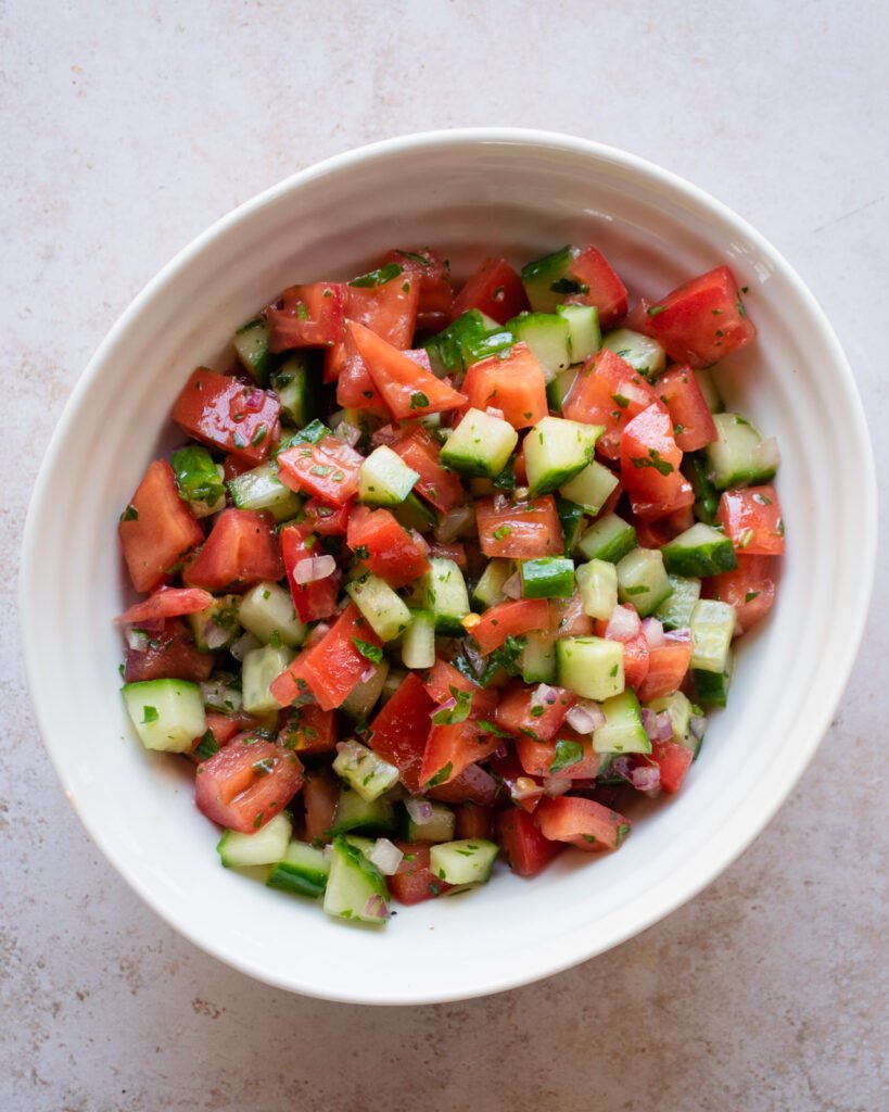 Tomato cucumber salad in a white bowl.