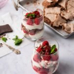 Two stemless wine glasses with chocolate eton mess inside and ingredients in the background.