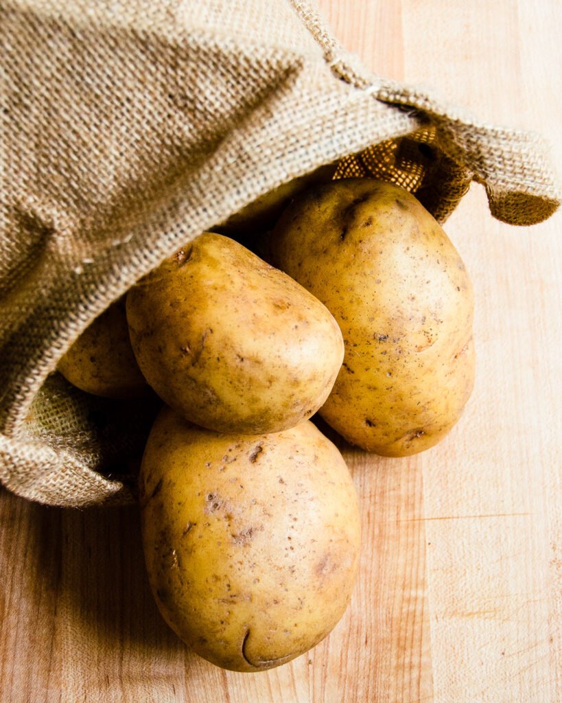 Yukon gold potatoes tumbling out of a burlap basket onto a wooden counter..