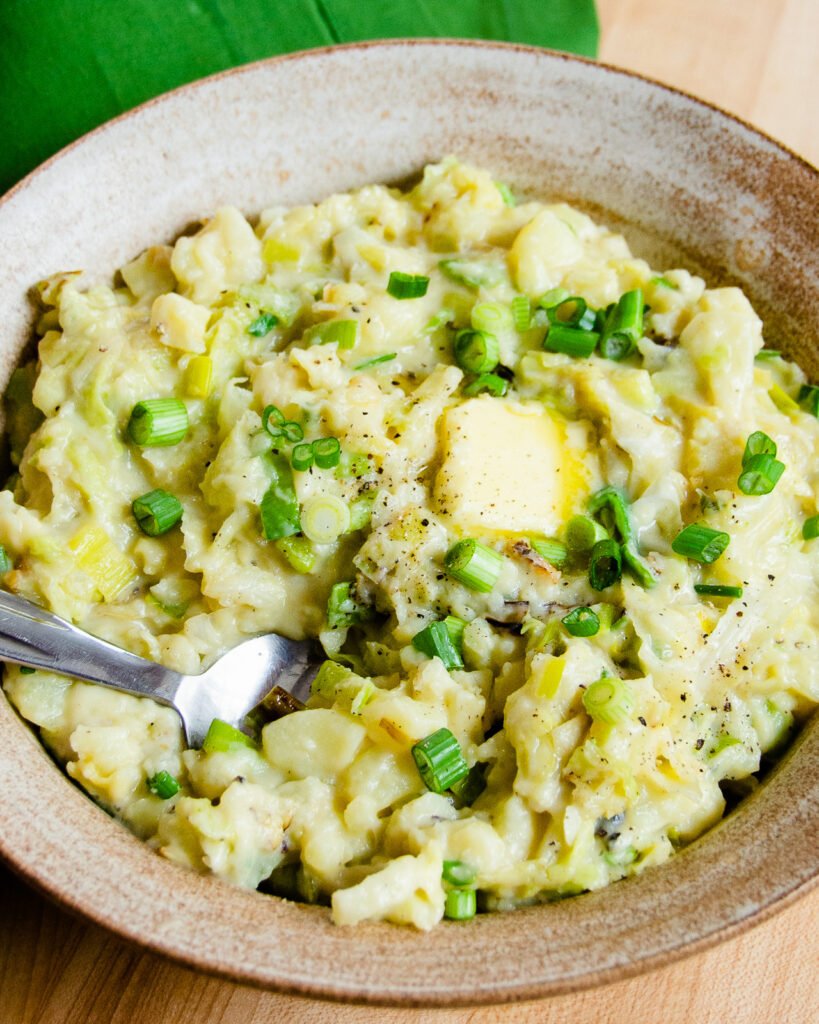 Colcannon in a brown ceramic bowl with a pad of butter melting on top and a green napkin on the side.