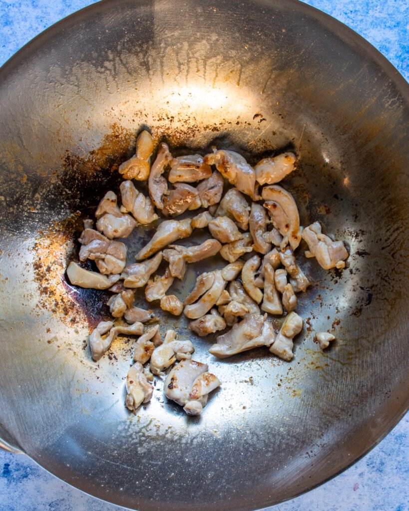 Chicken browning in the bottom of a wok.