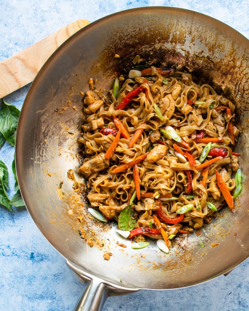 Drunken noodles in the bottom of a wok with a wooden spoon next to it.