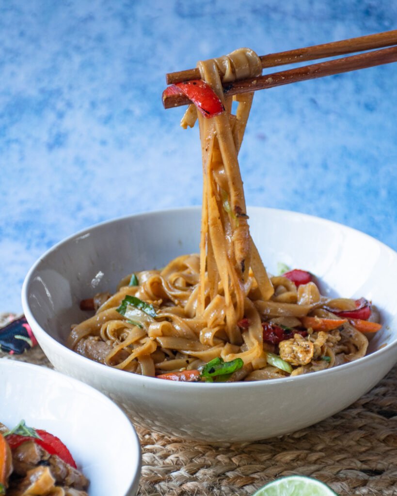 Chopsticks lifting drunken noodles out of a white bowl.