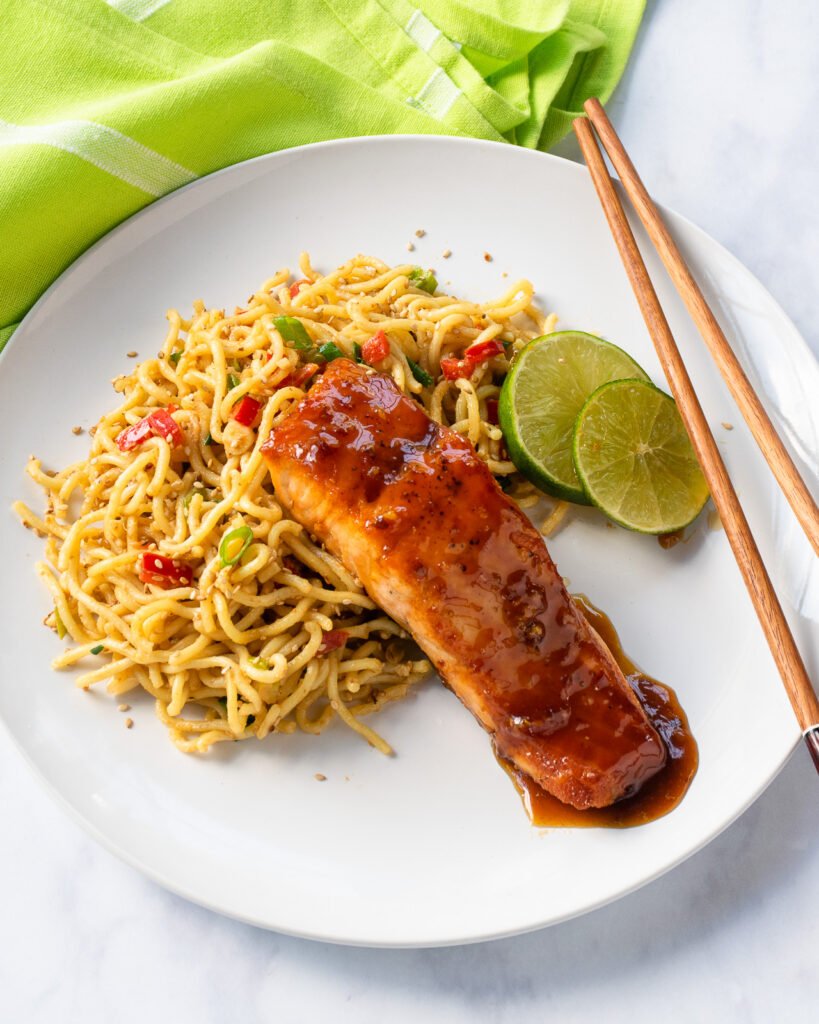 Honey soy salmon on a plate with sesame noodles and some chopsticks.