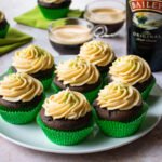 Irish Coffee Cupcakes in green cupcake liners on a plate with a bottle of Bailey's Irish Cream in the background.