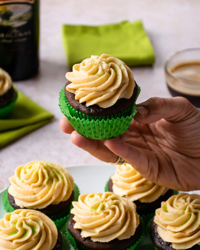 A hand holding up a single Irish Coffee Cupcake over a plate.
