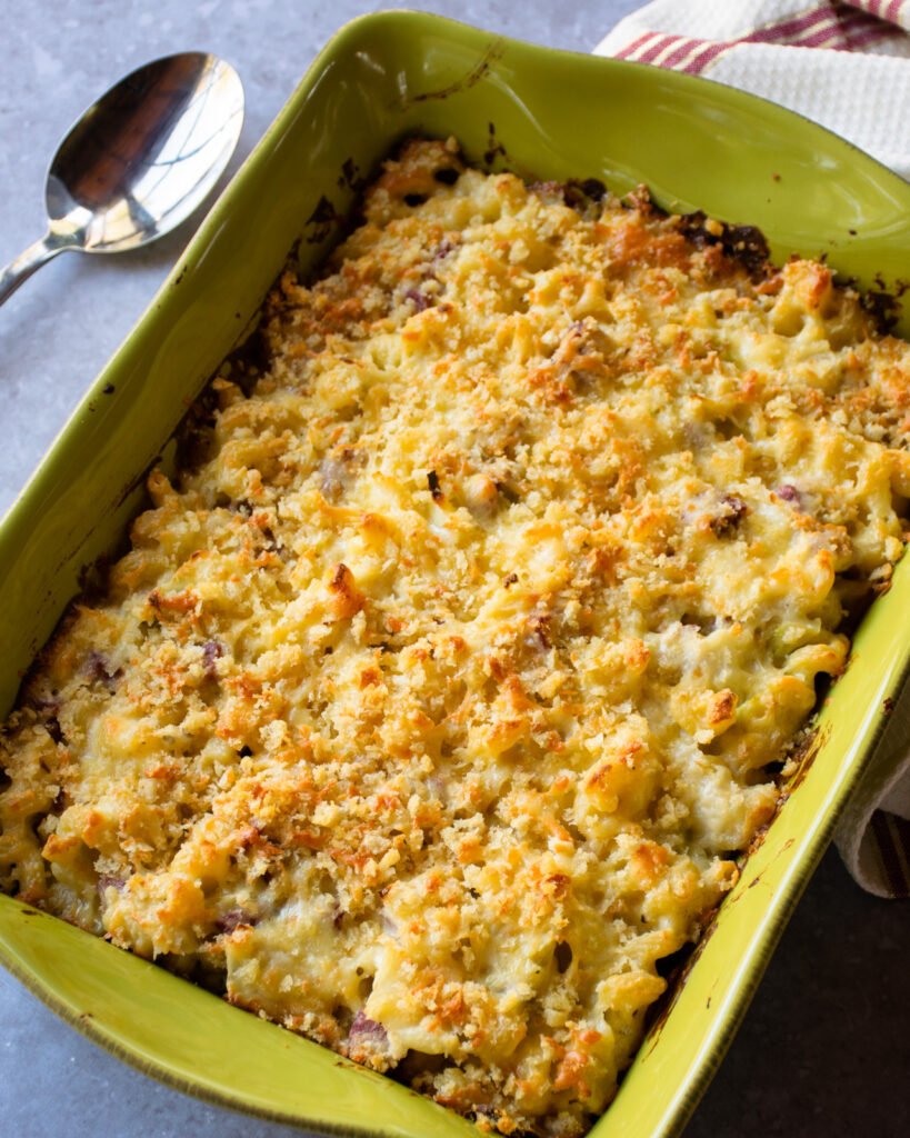 Irish Cheddar Mac and Cheese in a green casserole dish with a spoon and towel next to it.