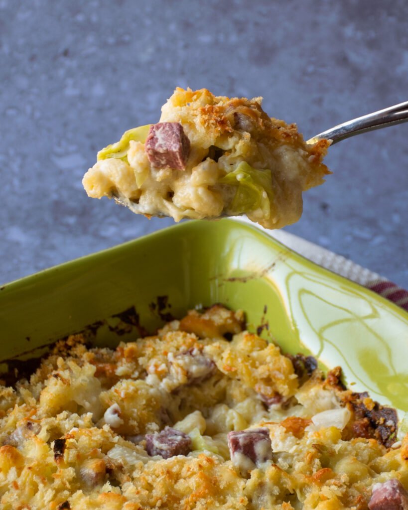 A spoon lifting up a portion of mac and cheese above a casserole dish.