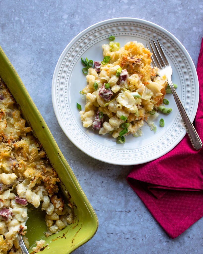 A plate of Irish Cheddar Mac and Cheese on a pink napkin with a green casserole dish next to it.