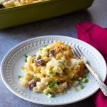 A plate of Irish Cheddar Mac and Cheese on a pink napkin in front of a green casserole dish.