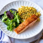 A fillet of pan roasted salmon on a white plate with rice and salad.