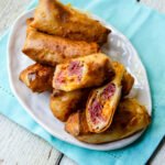 Reuben Egg Rolls on an oval white plate with a turquoise napkin underneaath.