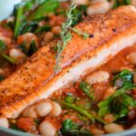Oven Roasted salmon with white beans and tomatoes in a skillet.