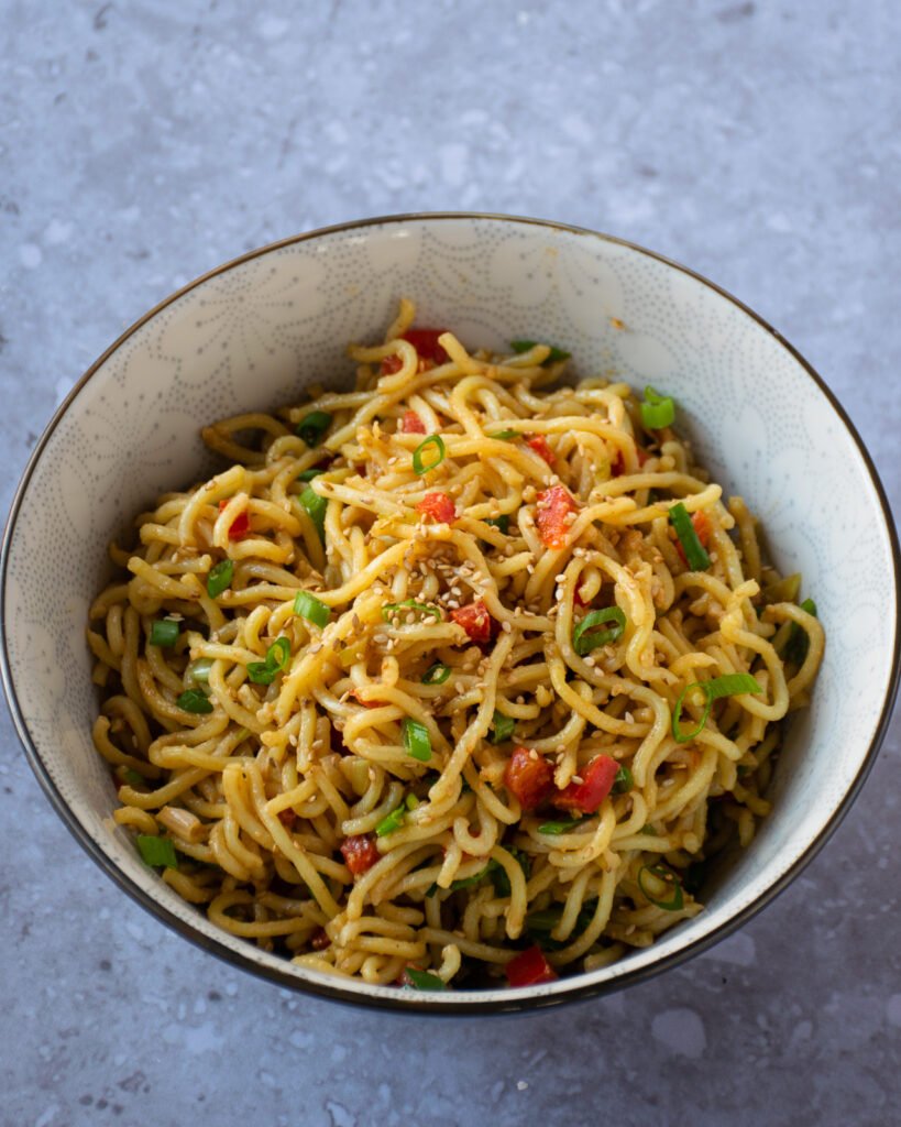 A bowl of sesame noodles on a grey counter.