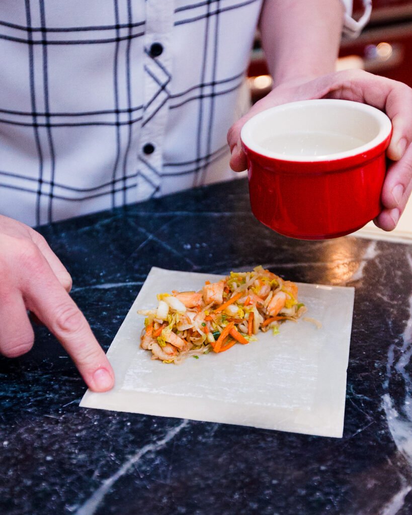 Brushing water on the edges of an egg roll wrapper with a finger.
