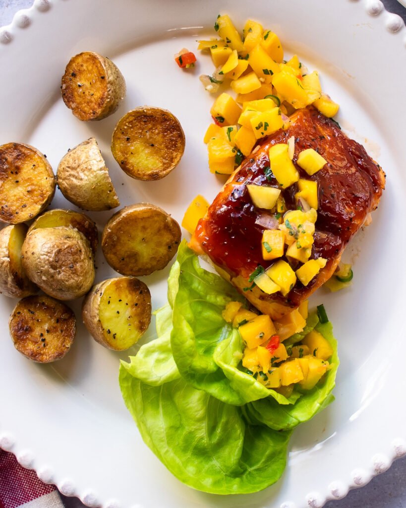 A dinner plate with potatoes, lettuce and salmon with mango salsa.