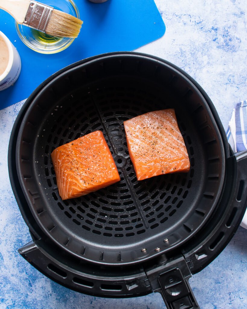 Two fillets of salmon in the basket of an air fryer with a blue background.