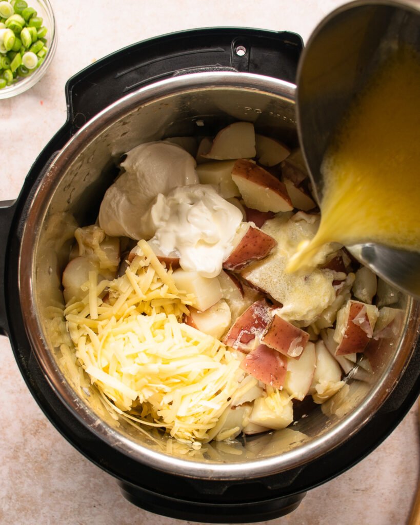 A saucepan pouring butter and cream into a pressure cooker with potatoes, cheese and sour cream in it.