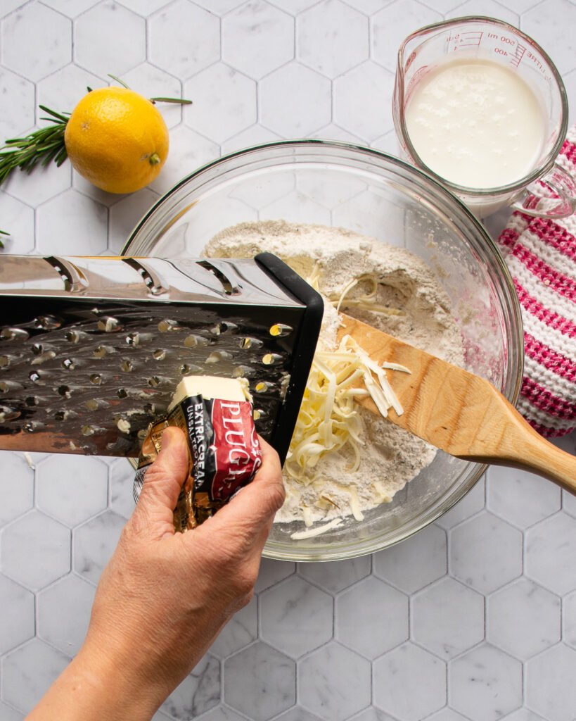 A hand grating butter into a bowl of flour.